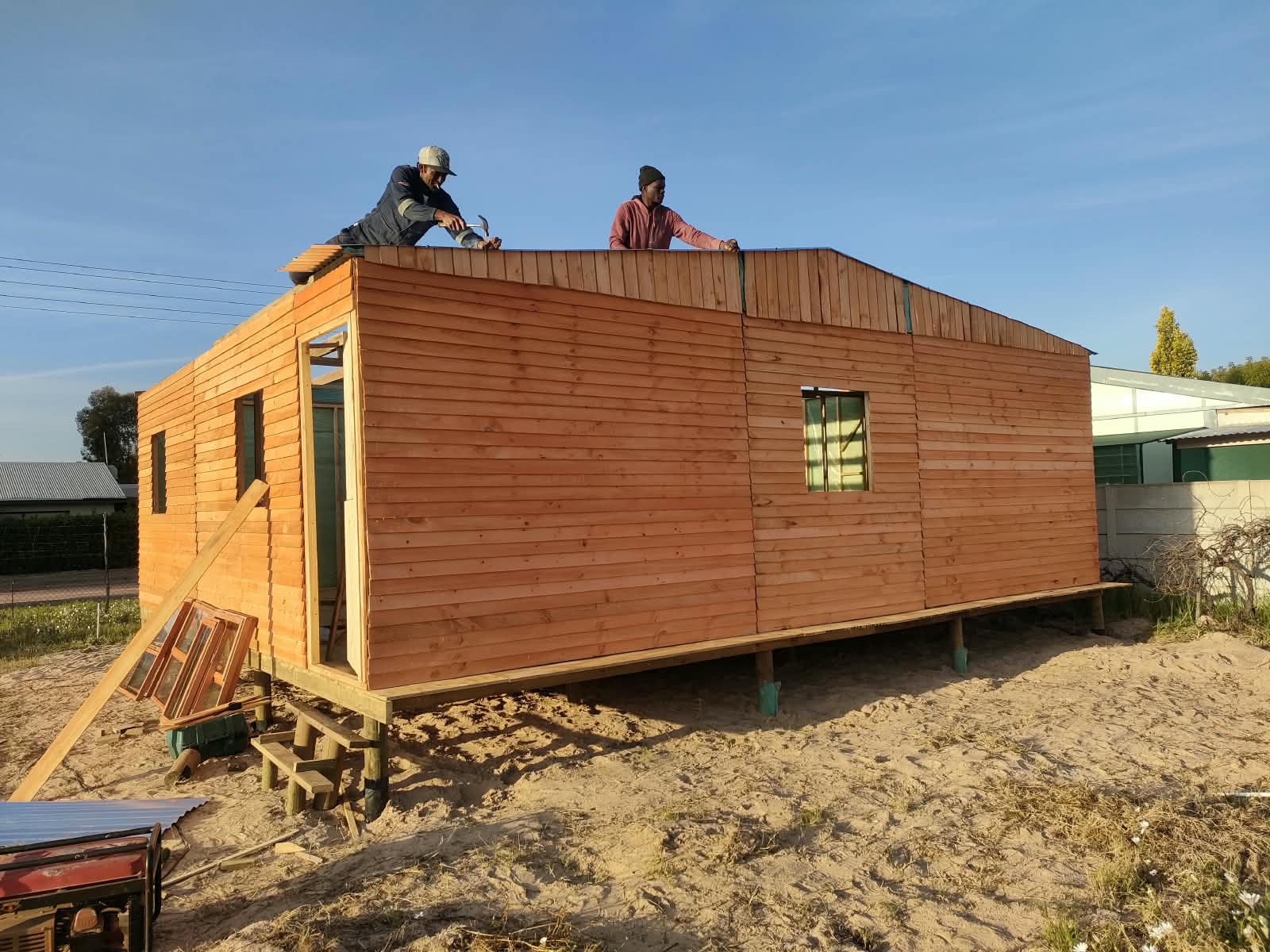 Two builders installing the roof on a large timber Wendy house under construction